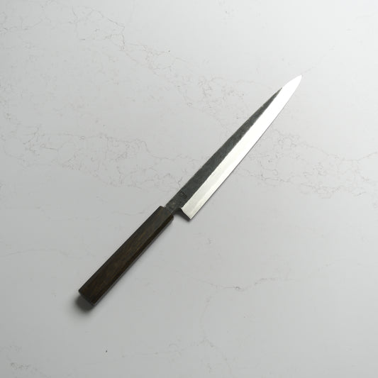 Sakai Kikumori Kikuzuki Kuro Yanagiba 270mm – Traditional carbon steel Japanese sushi knife with a kurouchi finish and octagonal handle. Handcrafted in Sakai, Japan. Available at Blade & Board.