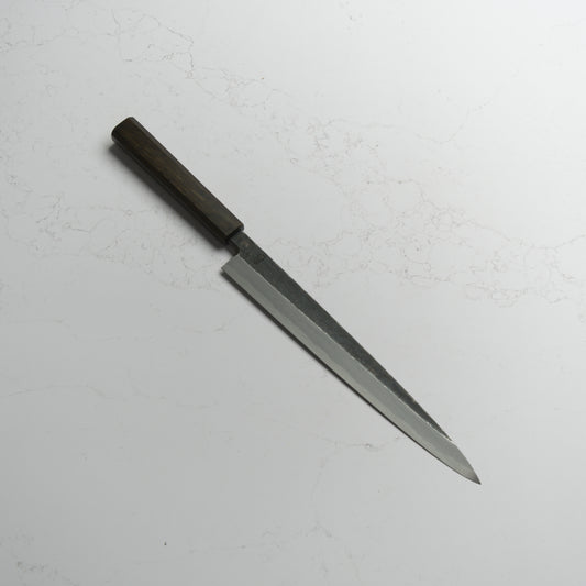 Sakai Kikumori Kikuzuki Kuro Yanagiba 270mm – Traditional carbon steel Japanese sushi knife with a kurouchi finish and octagonal handle. Handcrafted in Sakai, Japan. Available at Blade & Board.